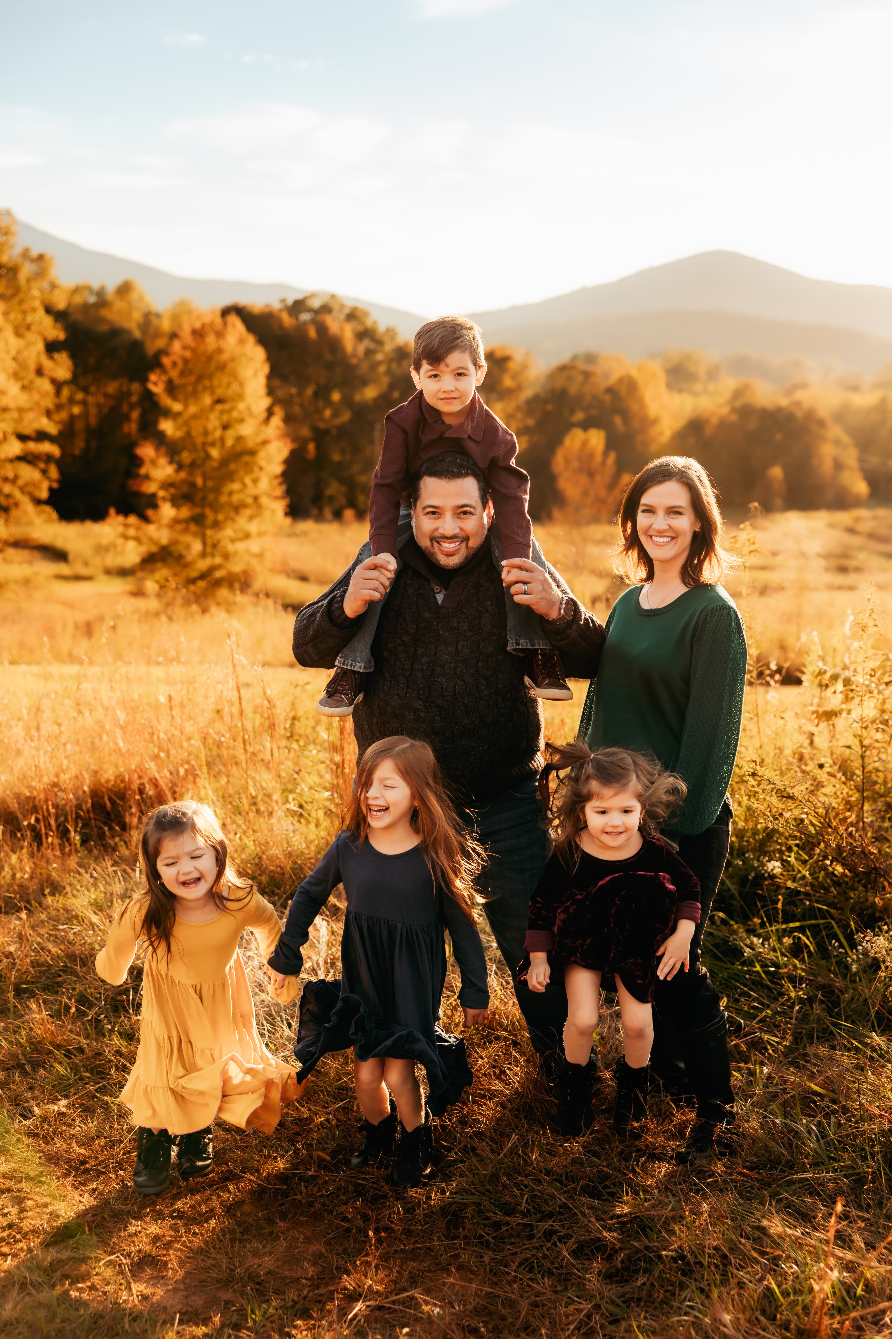 The Mastropasqua family in an autumn mountain field at golden hour. Fred with one of the twins on his shoulders, his wife on the right, and the three girls in front.